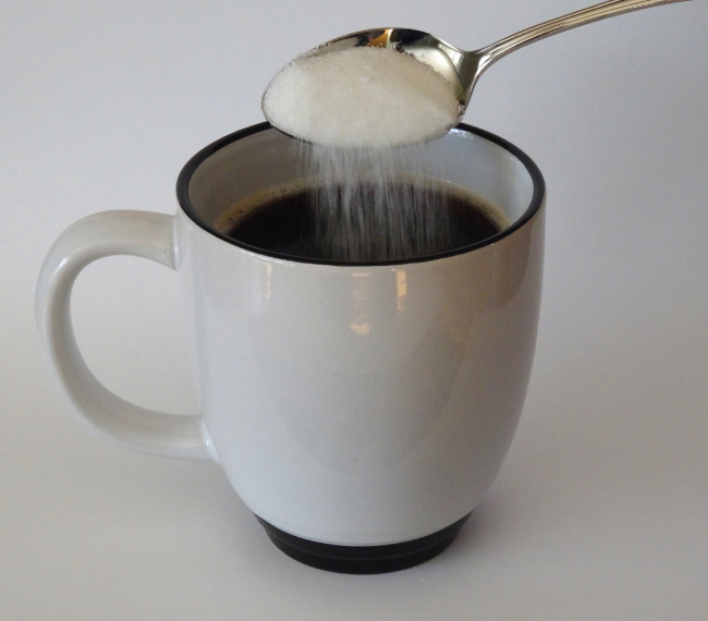 Une photo montre du sucre versé d'une cuillère dans une tasse.