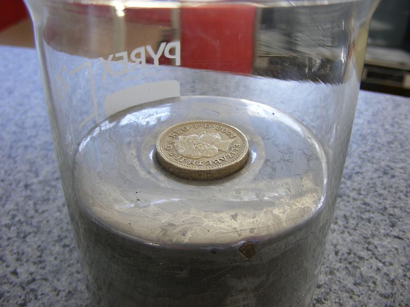 B. Una moneda descansa sobre la superficie de mercurio líquido en un vaso de precipitados.