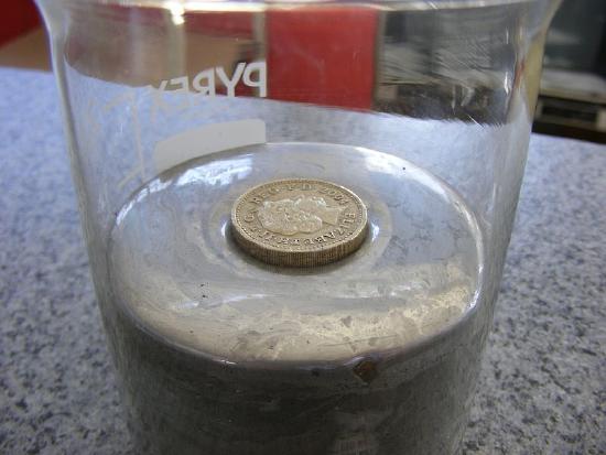B. A coin rests on the surface of liquid mercury in a beaker. 