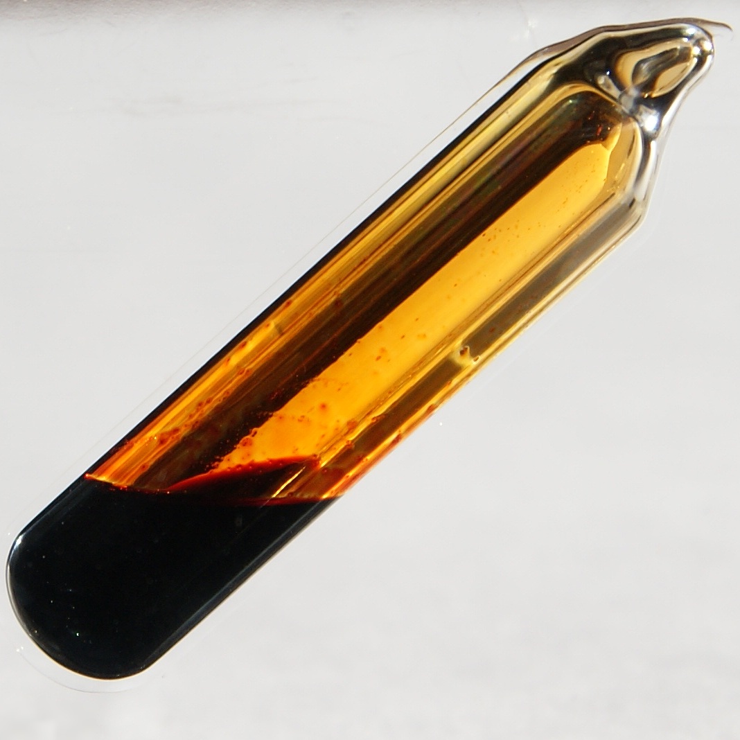 Cristalería cilíndrica llena de un líquido marrón oscuro profundo.