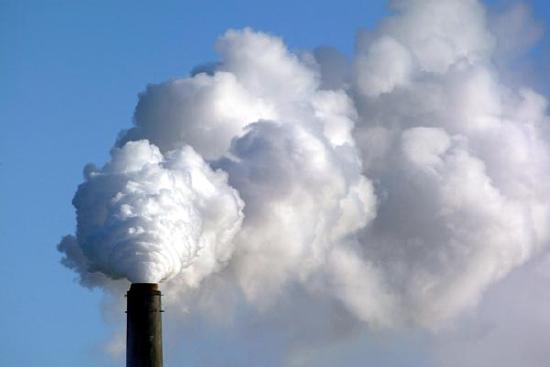 Large cloud of white vapor exits the chimney of a plant.