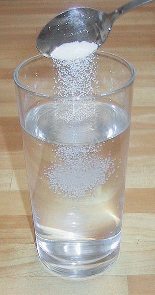 Cuchara vertiendo sal en un vaso de agua.