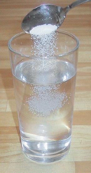 Spoon pouring salt into a glass of water. 