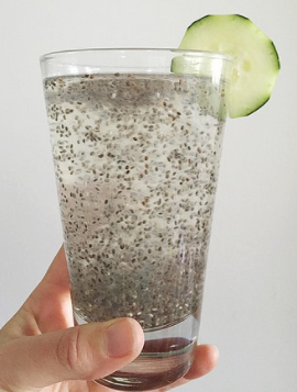 Image of a glass of water filled with chia seeds. There is a cucumber slice on the edge of the glass.