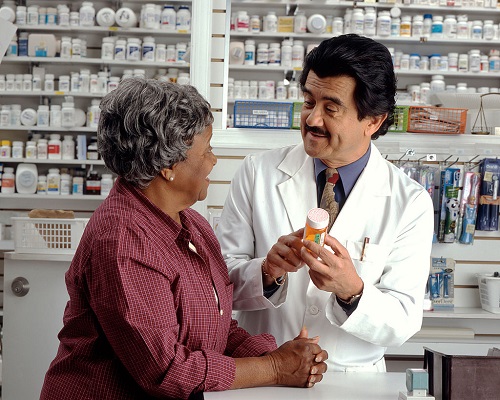 An older African-American woman talks to a Hispanic male pharmacist as he explains her prescription.