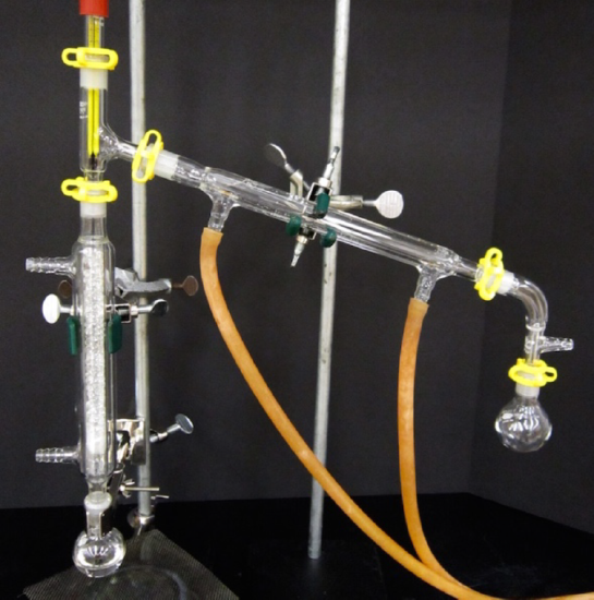 Vacuum distillation apparatus. A flask is connected to a long vertical condenser. The first condenser flows into a second condenser ending in another flask. Two outlet hoses attach to the bottom of the second condenser.
