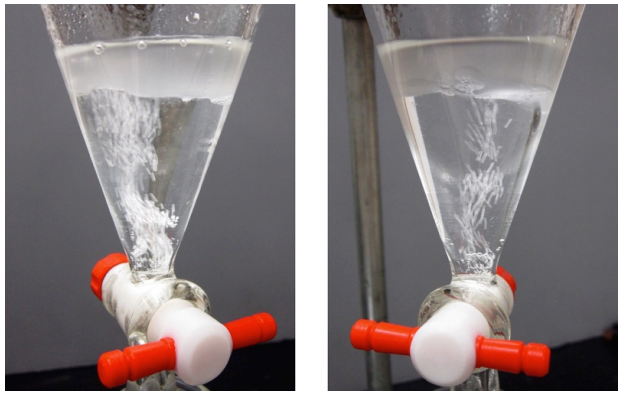   Funnel with boiling liquid. Liquid is separated into two layers: bottom clear layer of aqueous sodium bicarbonate and top, foggy layer of acid.