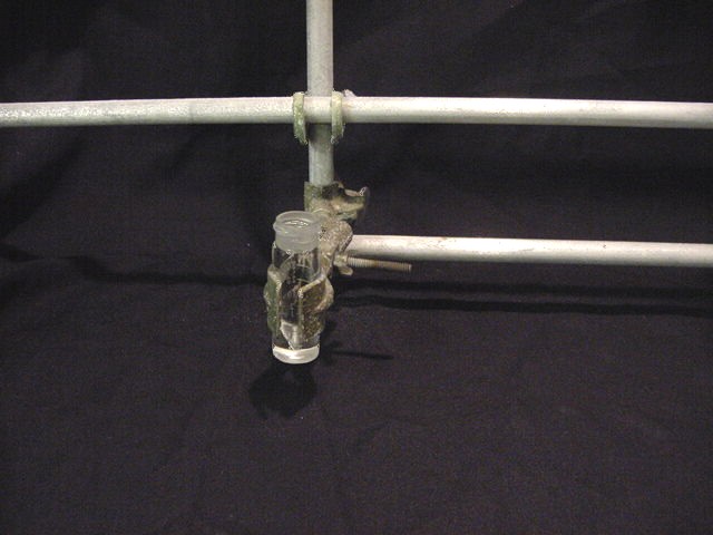A glass vial is held by a clamp.
