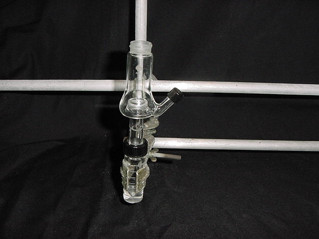 A Hickman still head is held in place with a clamp above a glass vial.