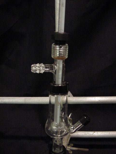 A Hickman still head is held in place with a clamp above a glass vial. A thermometer is placed into the Hickman still.