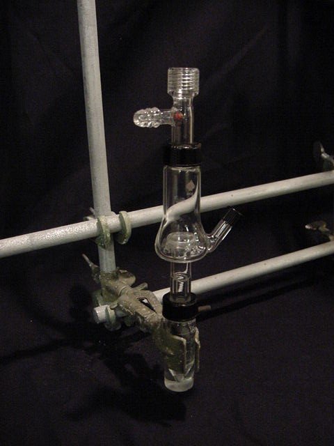 A glass vial is held by a clamp. A Hickman still is clamped above it with a condenser inside it.