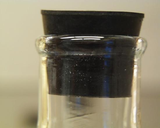 The opening of an Erlenmeyer flask is shown with a black stopper placed inside of it.