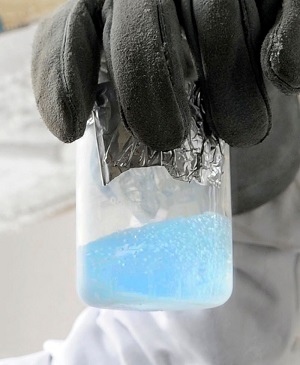 Liquid oxygen shown in a clear container being held by a person wearing thick gloves.