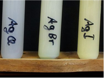 Tres tubos de ensayo. De izquierda a derecha: Líquido gris marcado con cloruro de plata; Líquido color crema con un toque de bromuro de plata etiquetado verde; Líquido amarillo marcado con yoduro de plata.