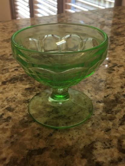 A vaseline glass sits on a countertop, it displays the characteristic appearance of uranium glass in its color.