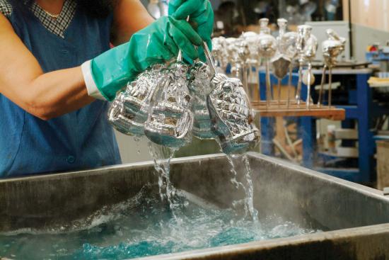 A person wearing gloves is holding a bunch of ornaments that she has just lifted from a basin containing a solution.  