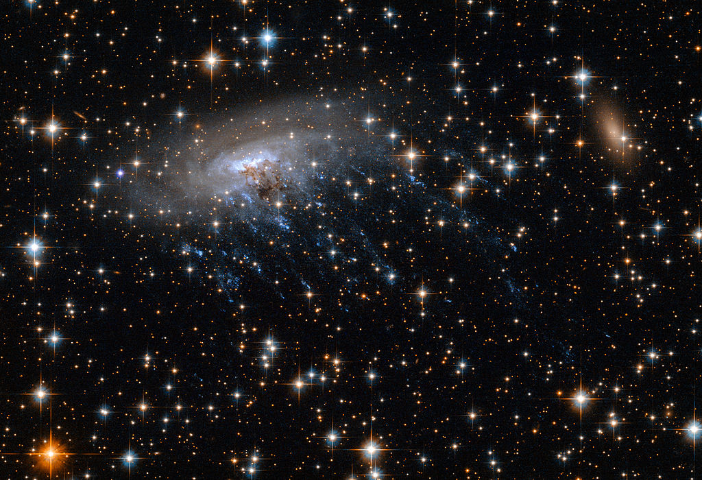 Image shows spiral galaxy ESO 137-001, framed against a bright background as it moves through the heart of galaxy cluster Abell 3627.