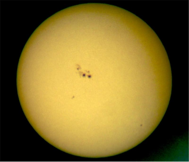 The sun in white light visible through a small telescope, with large group of sunspots near the center.