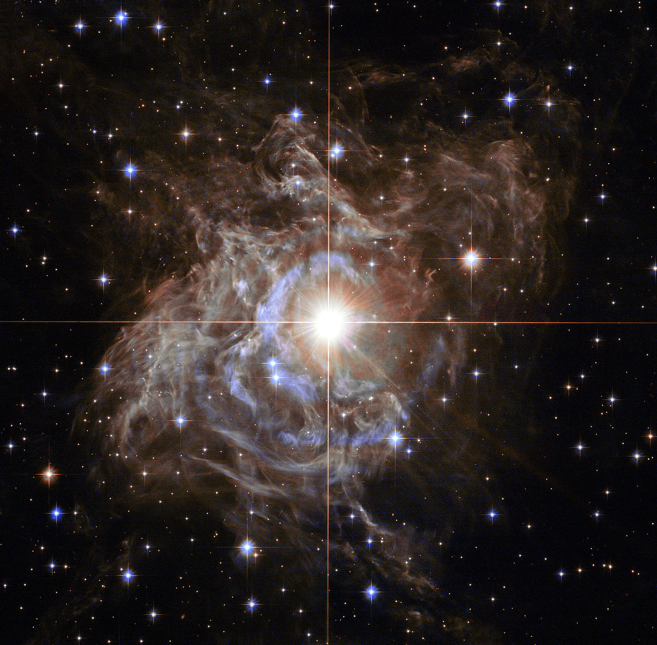 This Hubble image shows RS Puppis, a type of variable star known as a Cepheid variable. As variable stars go, Cepheids have comparatively long periods— RS Puppis, for example, varies in brightness by almost a factor of five every 40 or so days. RS Puppis is unusual; this variable star is shrouded by thick, dark clouds of dust enabling a phenomenon known as a light echo to be shown with stunning clarity. These Hubble observations show the ethereal object embedded in its dusty environment, set against a dark sky filled with background galaxies.