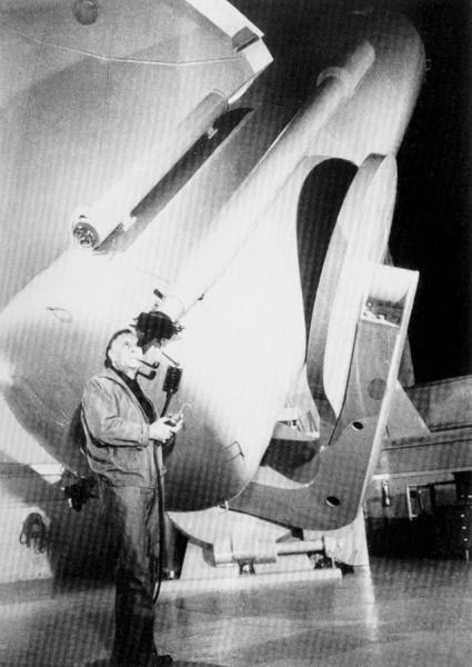 Black and white image of Edwin Hubble standing by the 100-inch Mt. Wilson Telescope at the Mt. Wilson Observatory.