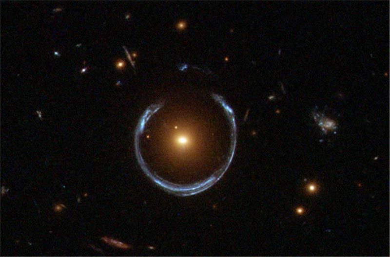 The gravity of a luminous red galaxy, center, has gravitationally distorted the light from a much more distant blue galaxy, seen as a horseshoe surrounding the luminous red galaxy. Rings like this are now known as Einstein Rings.