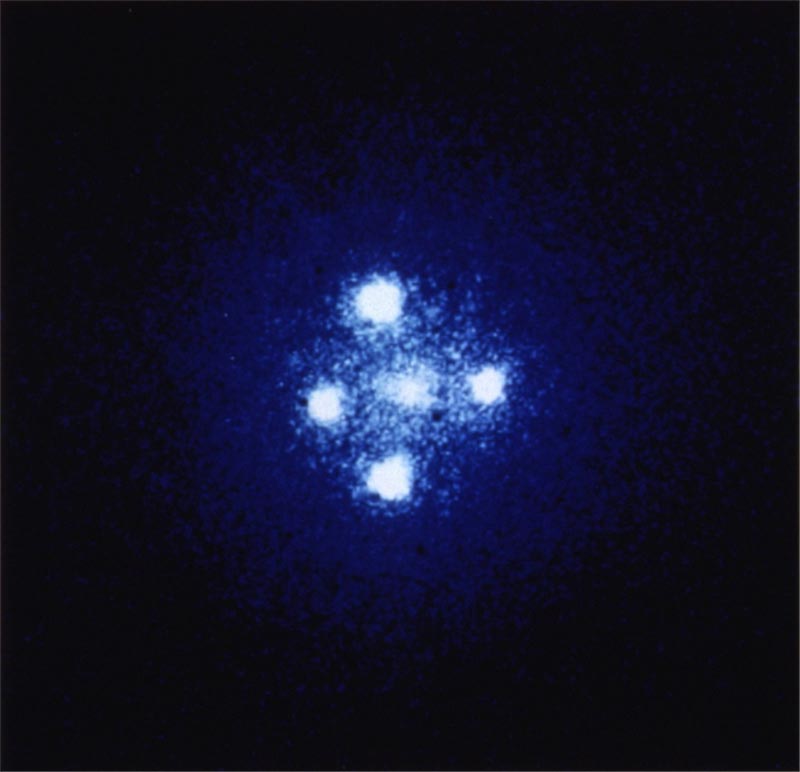 Formation known as Einstein’s Cross; four images of the same distant quasar appear around a foreground galaxy due to strong gravitational lensing of that galaxy in the foreground.