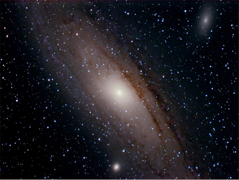 Image of The Andromeda Galaxy with two companion galaxies; dark lanes within a broad band of stars are dust lanes within the Milky Way Galaxy.