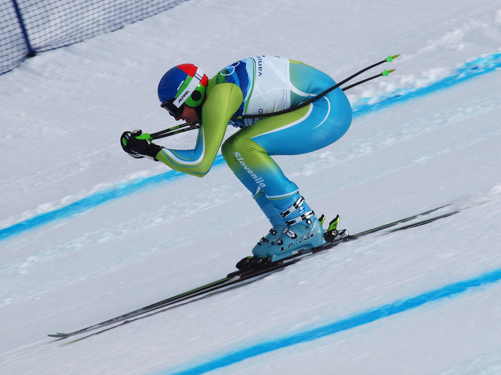 Skier in a tucked position, racing downhill.