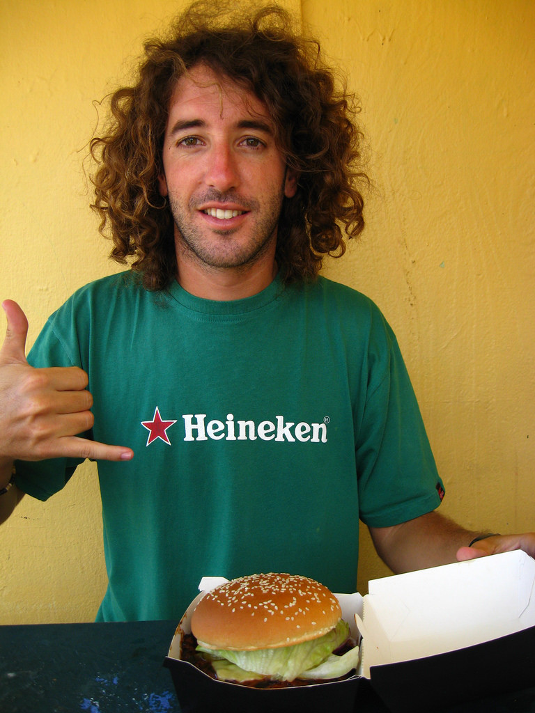 Photo of a young man enthusiastically pointing to a hamburger in a takeout box.