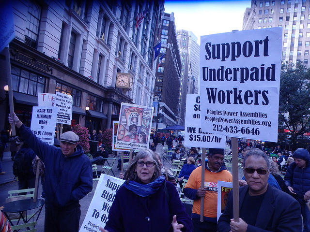 Protestors holding placards at a NYC rally to raise the minimum wage. A sign in the forefront reads, "Support Underpaid Workers."