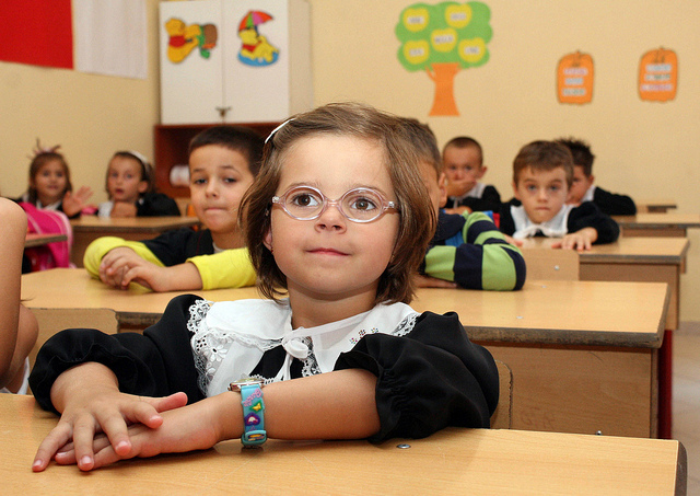 Photograph of wide-eyed and eager children on their first day of school, sitting at their desks in a classroom.