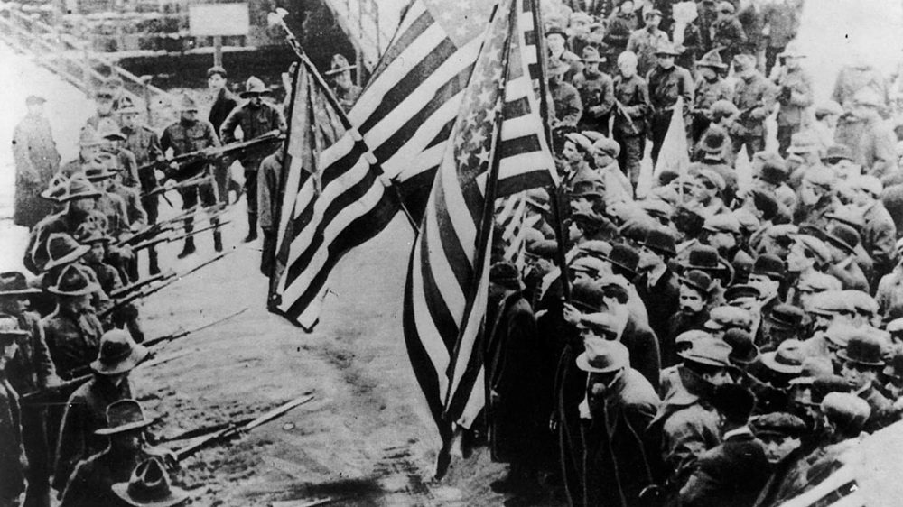 Photo of strikers, carrying American flags, confronting strikebreakers and militia bayonets.