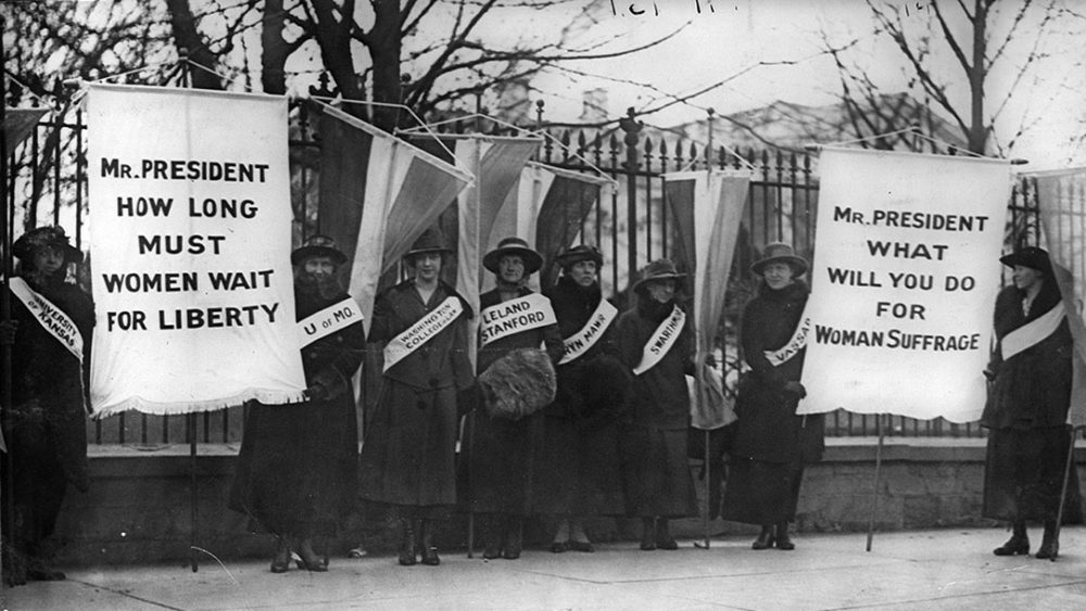 Suffragettes picket with signs saying, "Mr. President how log must women wait for liberty?" and "Mr. President what will you do for woman suffrage?"