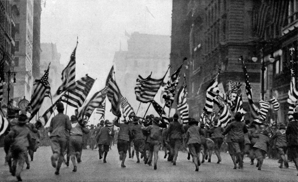 Boy Scouts carry American flags while running in the street for a parade.