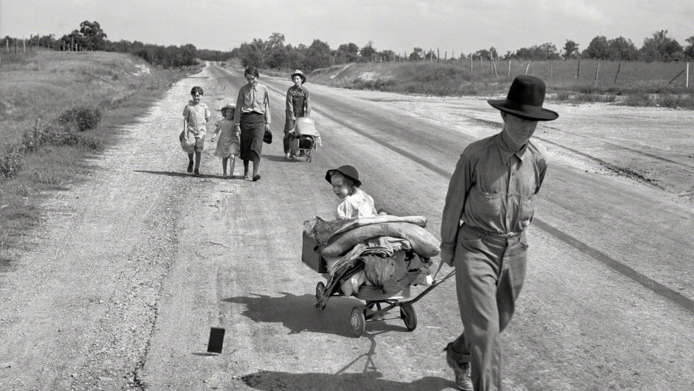 Man pulling his child in a wagon as his wife and four other children follow behind on the road.