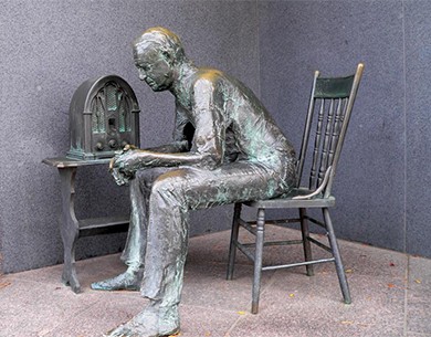 A sculpture shows a man sitting in a chair beside a radio.