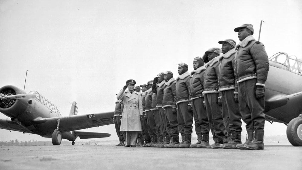 Tuskege Airmen (African-American pilots) stand at attention in front of their aircraft.