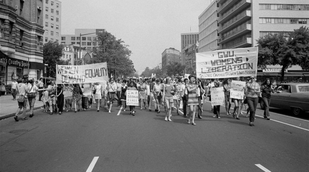 Women walk the streets of Washington with signs saying "Women Demand Equality" and "GWU Women's Liberation"