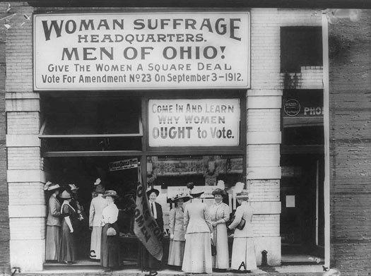 This photo shows several women outside of the Woman Suffrage Headquarters. A large sign reads