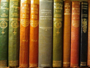 Leather-bound books on a shelf, including works by Sir Walter Scott and Charles Dickens