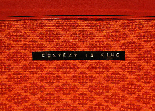 Red patterned background. Small black label tape central, reading "Context is King"