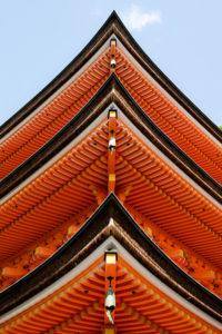 Looking up from below the corner of a Japanese temple, so that three levels of red eaves, capped by black gutters, are arranged in a strong vertical point