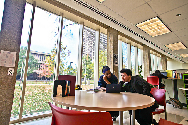 Two college students looking at a laptop at a circular table in a campus writing center