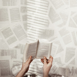 A pair of hands holding an open book against a background of blurred printed pages