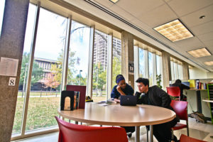 Two students sitting at a round table in front of a bank of windows