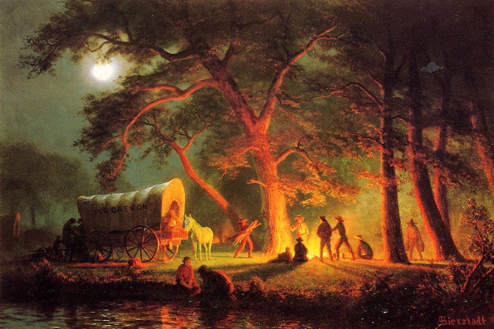 A group of people and a covered wagon by a fire in the middle of the woods at night.