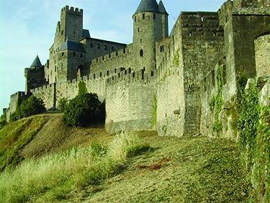 A photograph shows the medieval walled city of Carcassonne. It is surrounded by a high double wall with slots at the top, likely for archers or other defenders to use, and it incorporates several round parapets with narrow window openings.
