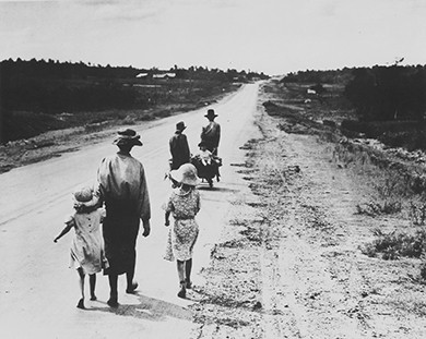 A photograph shows six Dust Bowl refugees—three adults, two children, and a baby—walking down a road. The baby rides in a small wagon.