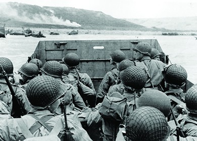 A photograph shows U.S. troops in a military landing craft approaching a beach. Ships are visible in the far distance.