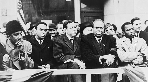 A photograph shows Bayard Rustin, Andrew Young, William Fitts Ryan, James Farmer, and John Lewis sitting in the front row of a large group of people.